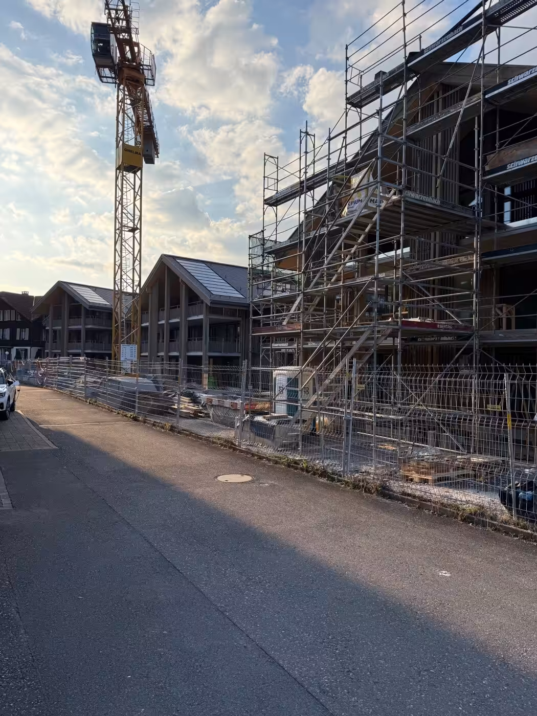 Mehrfamilienhäuser im Bau bei Sonnenschein, mit Baugerüst und Kran im Hintergrund.