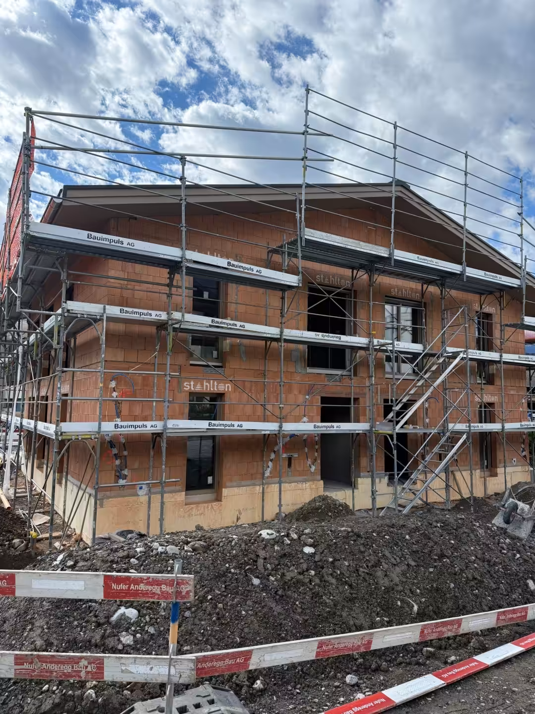 Rohbau eines Hauses mit Gerüst und Bauarbeiten unter bewölktem Himmel.
